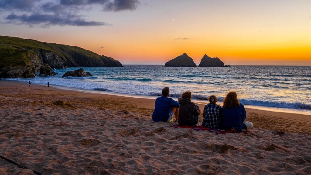 A group gathers to enjoy the sunset over the Gull Rocks at Holywell Bay Beach, Cornwall